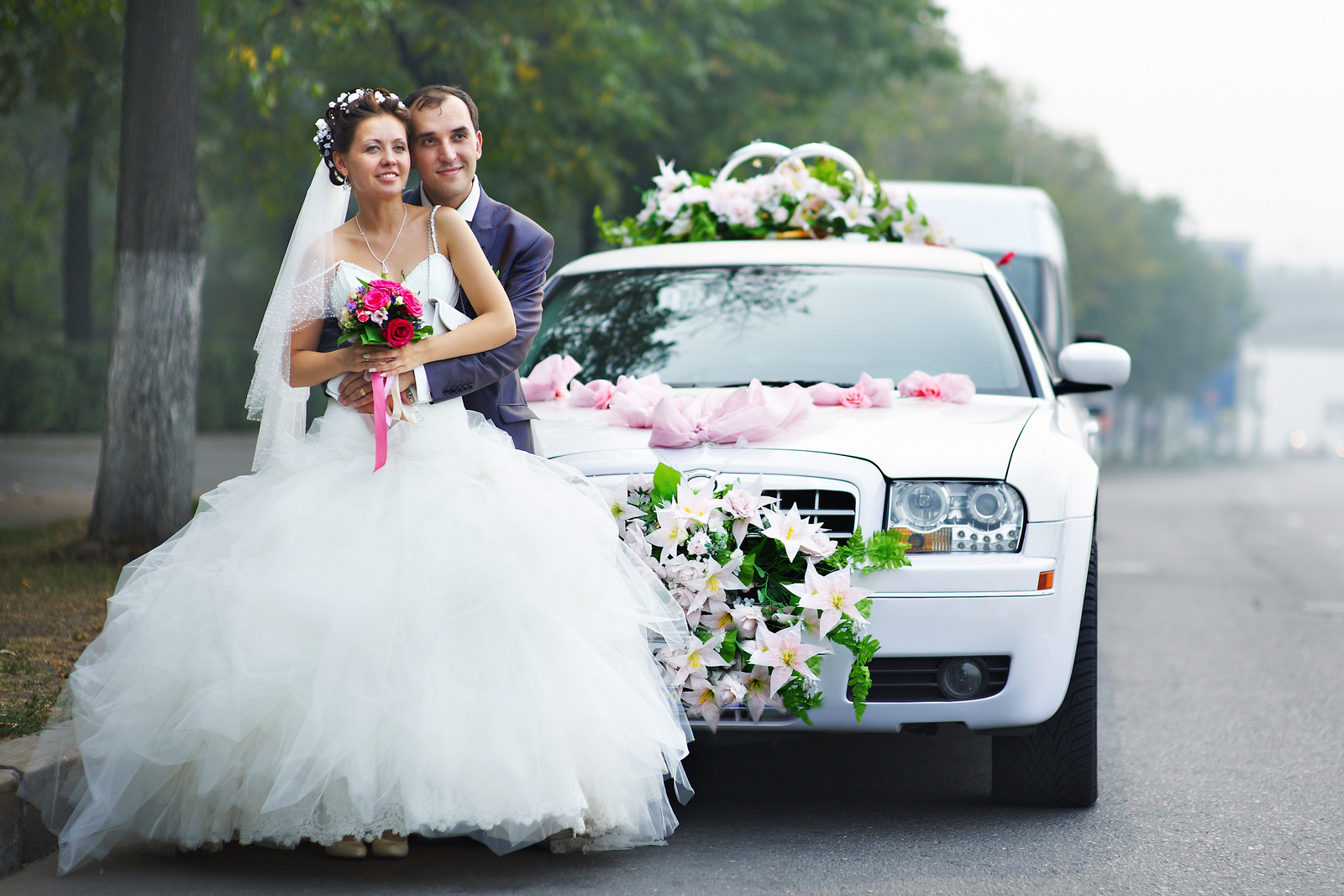Bride and groom posing with decorated white wedding car — luxury wedding transportation St Augustine FL